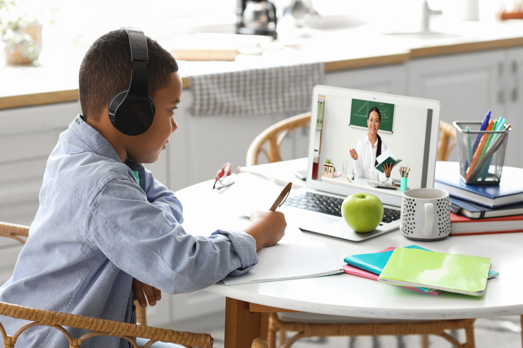 Boy doing online school at a desk wearing headphones looking at laptop